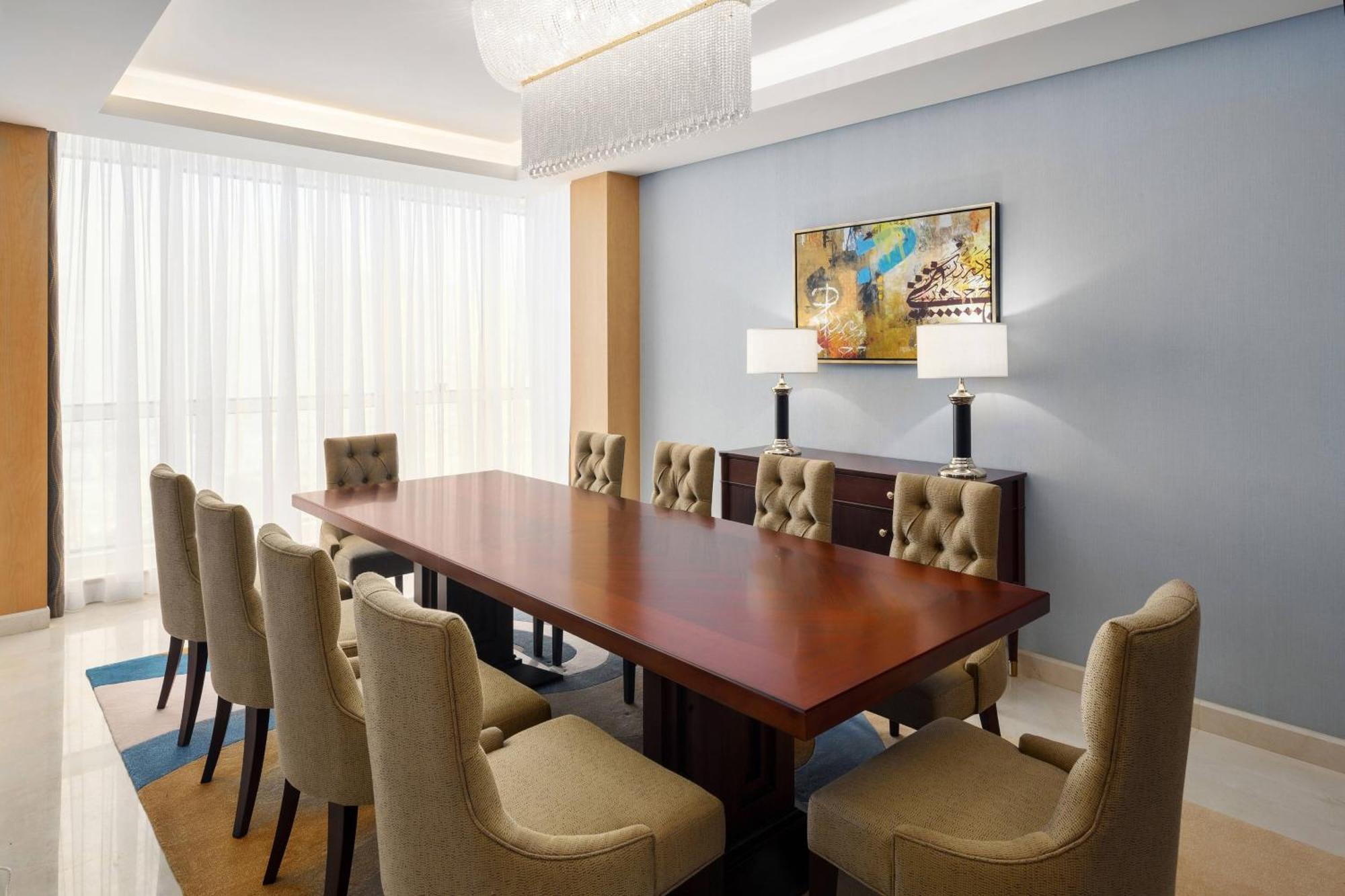 Sheraton Makkah Jabal Al Kaaba Hotel Mekka Exterior foto The photo shows a spacious and elegantly designed conference room. It features a large wooden conference table surrounded by upholstered chairs. The chairs have a beige color and a tufted design. On one side of the room, there are two contemporary la